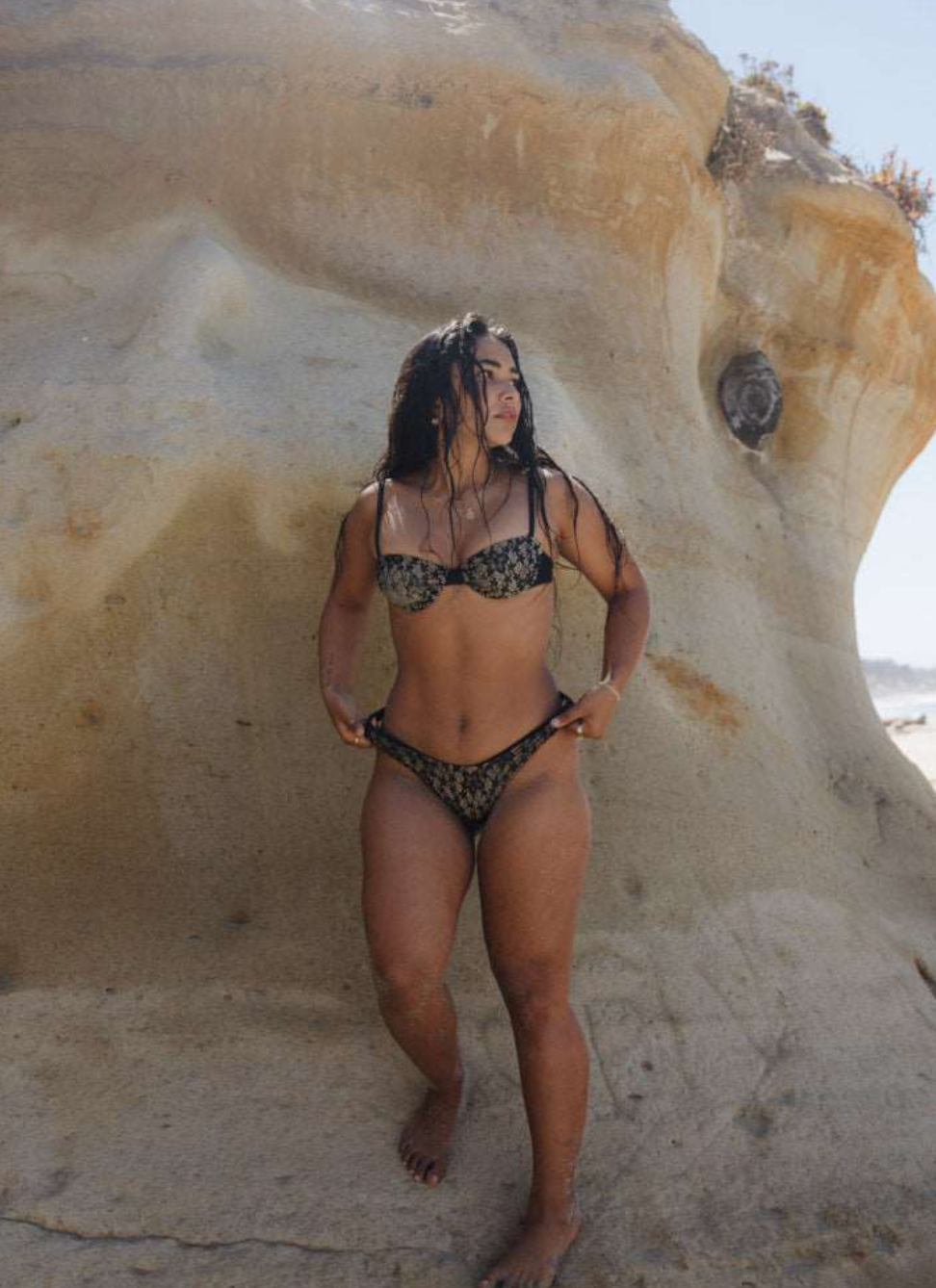 Woman in a black lace bikini standing against a rock formation.